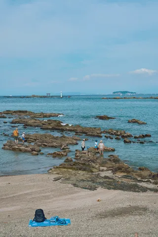 磯で遊ぶ人たちと、砂浜に広げられた青いレジャーシート
