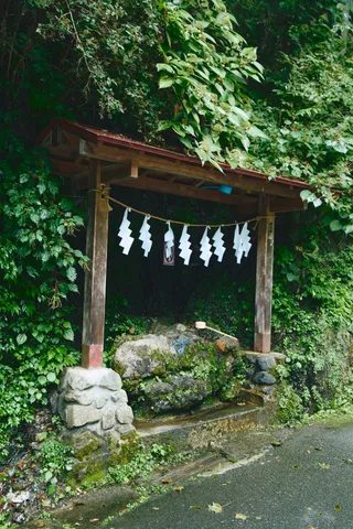 木の茂る崖下に立つ小さな鳥居と、注連縄の下の湧き水