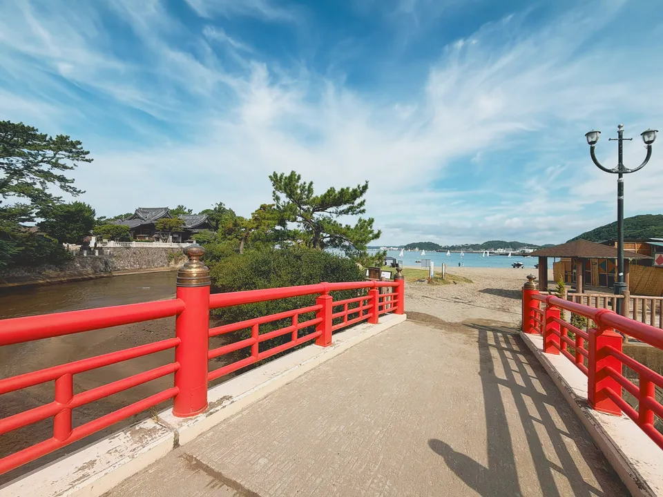 赤い欄干の橋の先に広がる砂浜と海