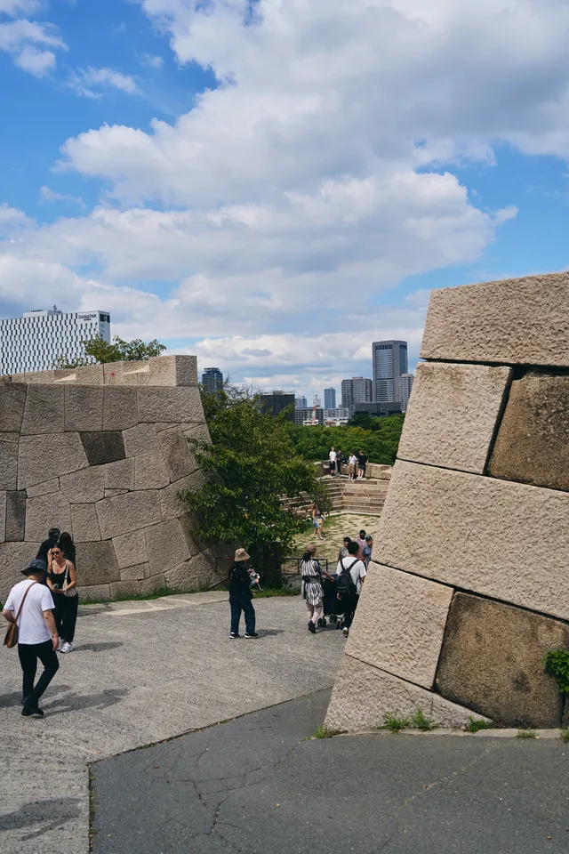 巨大な石垣のあいだを抜ける坂道と、遠くのビル群