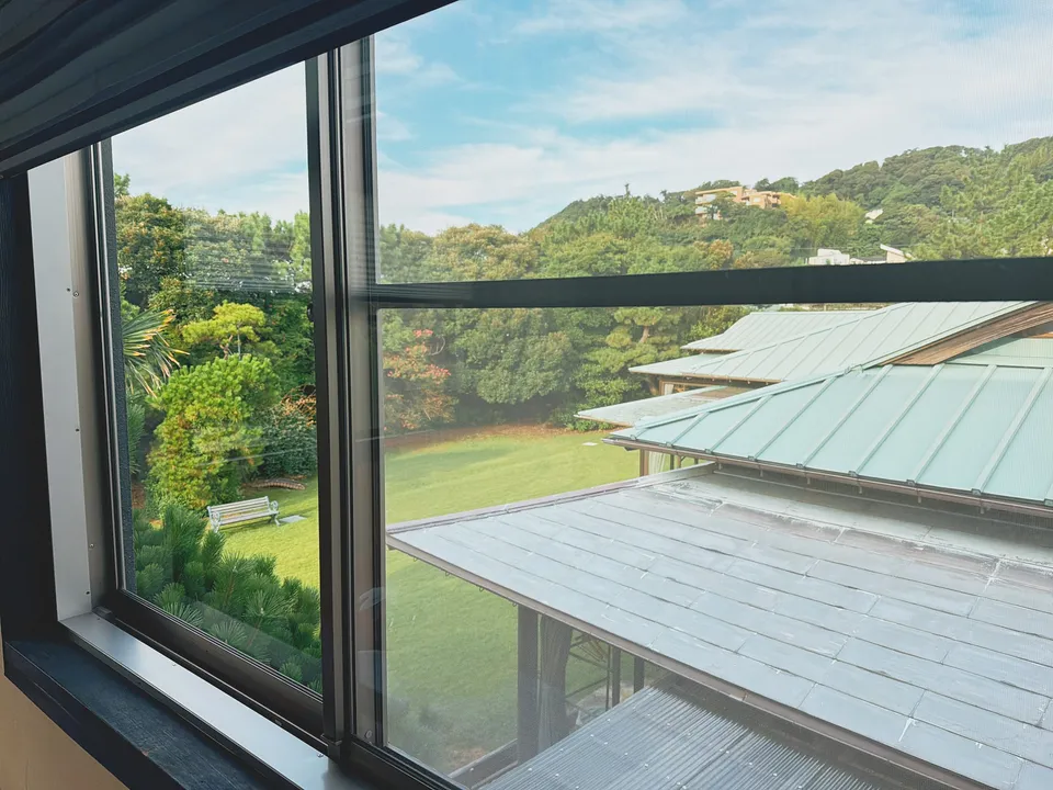 窓越しに見える、緑青色の屋根と芝生、その先の山