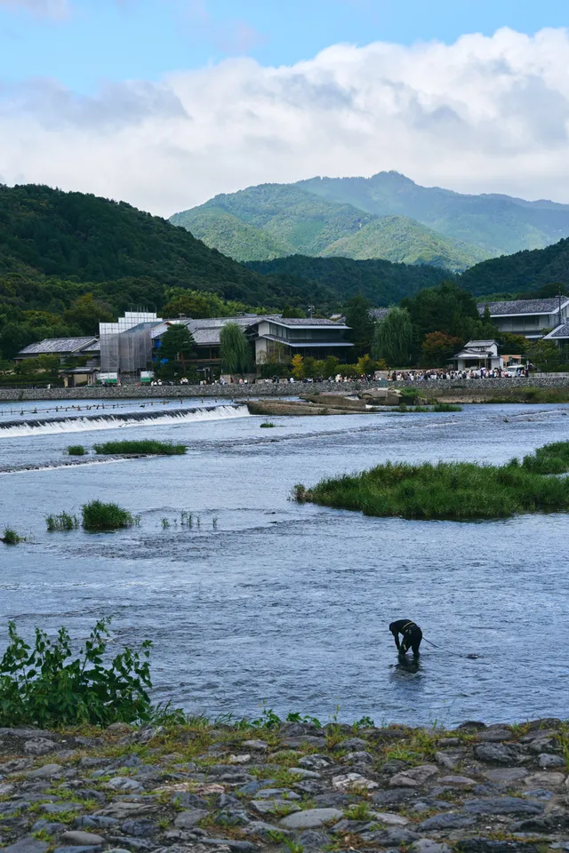 堰のある広い川と奥に連なる山、川の中に立つ人