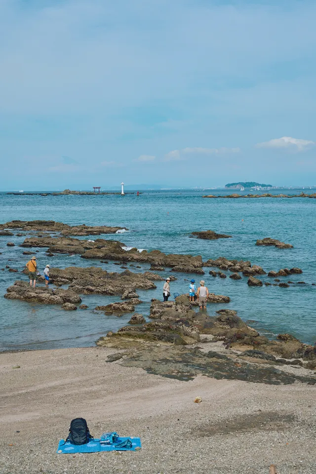 磯で遊ぶ人たちと、砂浜に広げられた青いレジャーシート