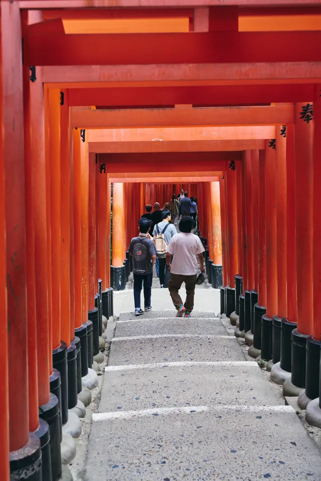 朱色の鳥居が続く石段と、上っていく人たち